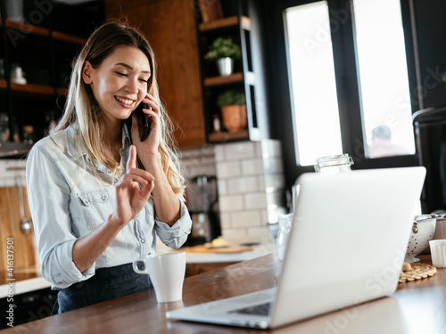 Beautiful woman drinking coffee and using the phone in the kitchen. Young woman talking to the phone.