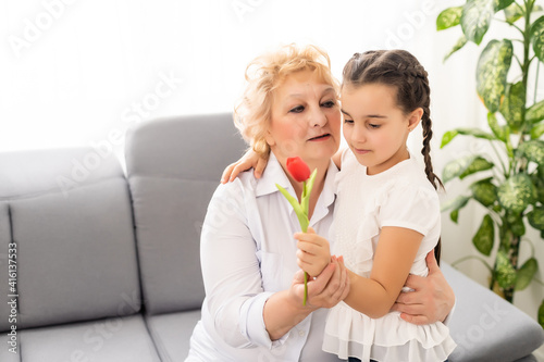 Congratulations concept. Congratulations on the holiday. The granddaughter gives flower to her grandmother on March 8th. International Women s Day. Grandmother and granddaughter with flower