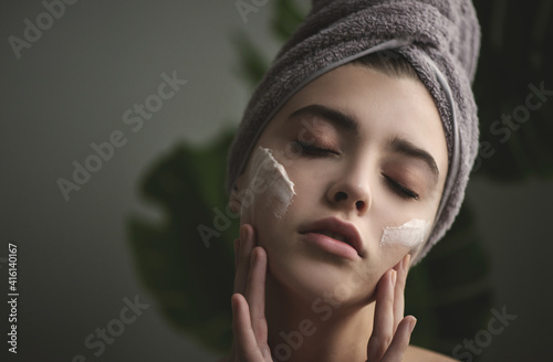 Young woman applying face cream on her face.