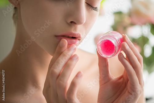 Beautiful young woman with clean perfect skin uses lips sugar scrub.