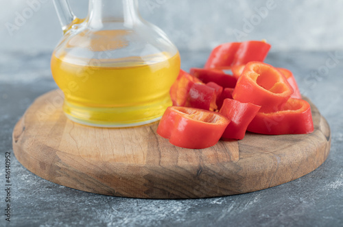 Sliced of sweet bell red pepper with a glass bottle of oil on a wooden board