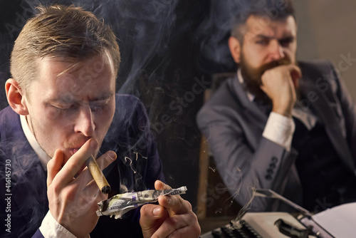 Man lighting cigar from burning dollar banknote. Business meeting. Gangster and money. Concept of crime. Smoky background. Retro and vintage style.