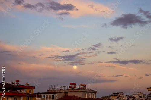 Moon between the clouds and the buildings with the sunset view