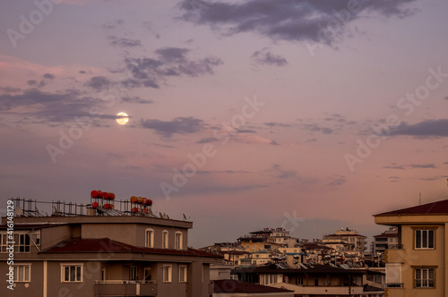 Moon between the clouds and the buildings with the sunset view