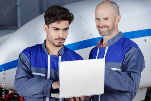 two modern mechanics working in hangar with laptop