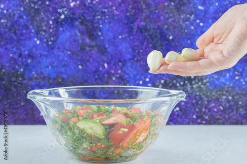 Hand adding garlic cloves into bowl of vegetable salad