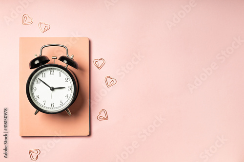 Alarm clock on pink background with diary
