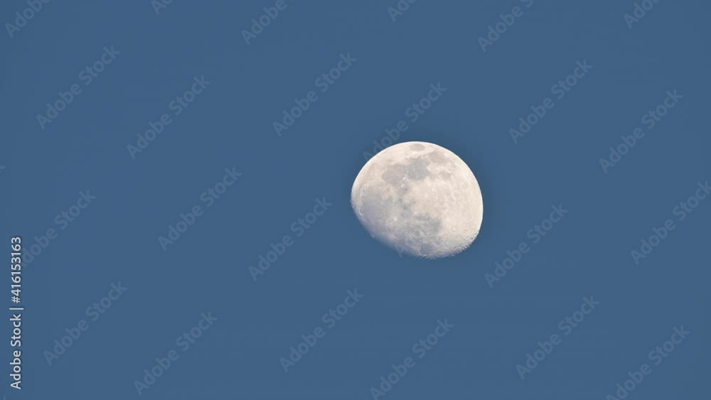 Stunning view of a bright half full moon moving on a dark blue sky.