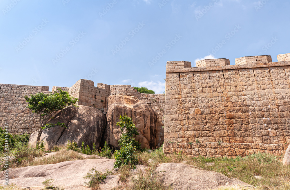 Chitradurga, Karnataka, India - November 10, 2013: Fort or Elusuttina Kote. Brown stone rampart walls with huge boulders against under blue sky. Some green foliage.