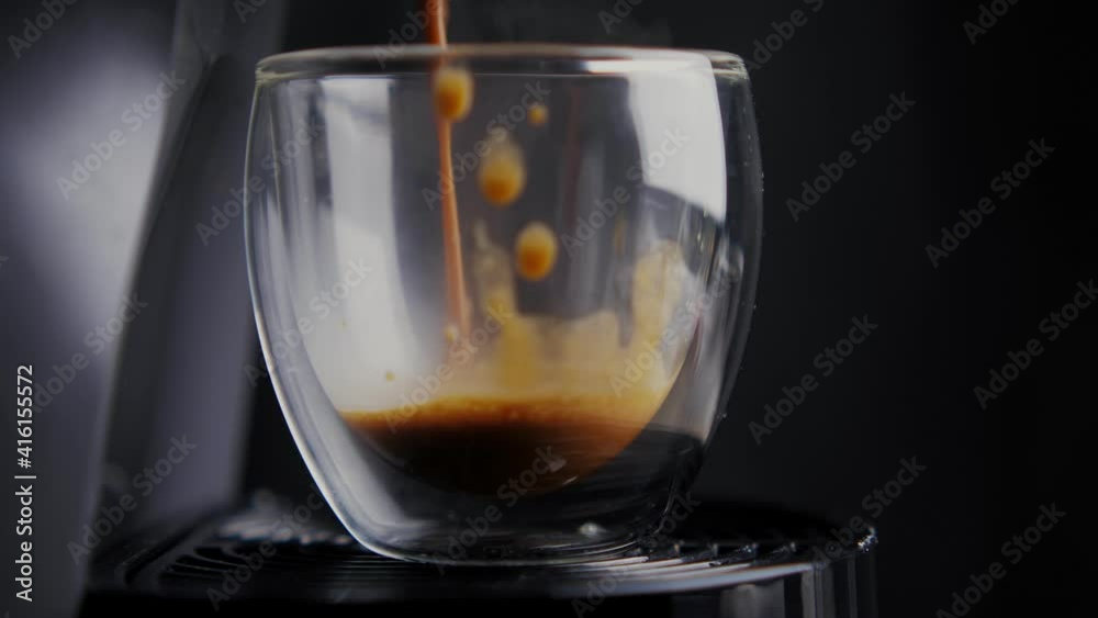 A cup is in the coffee machine and black coffee is being poured into it. Isolated on black background