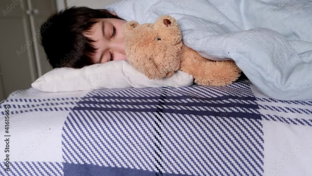 kid, a boy of 8 years old lies in bed, gently hugs a teddy bear with his hand, focus on the toy, concept of anxious sleep in schoolchildren, insomnia, night fears kid, a boy of 8 years old lies in bed, gently hugs a teddy bear with his hand, focus on the toy, concept of anxious sleep in schoolchildren, insomnia, night fears