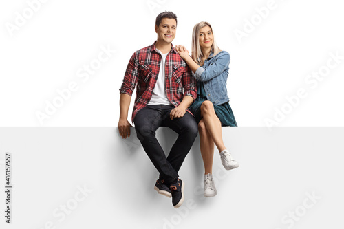 Smiling young couple sitting on a blank panel
