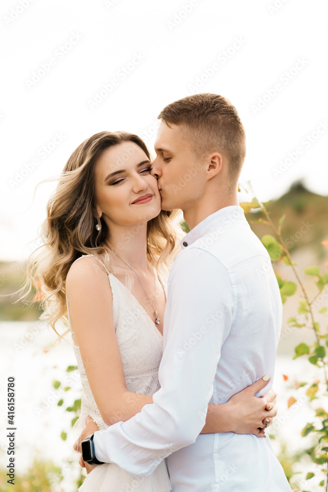 A beautiful young couple in love, a man and a woman embrace, kiss near a blue lake and sand at sunset. Vacation at the sea on the beach, sunset, morning, honeymoon, tropics, ocean, girl, relationship. A beautiful young couple in love, a man and a woman embrace, kiss near a blue lake and sand at sunset. Vacation at the sea on the beach, sunset, morning, honeymoon, tropics, ocean, girl, relationship.