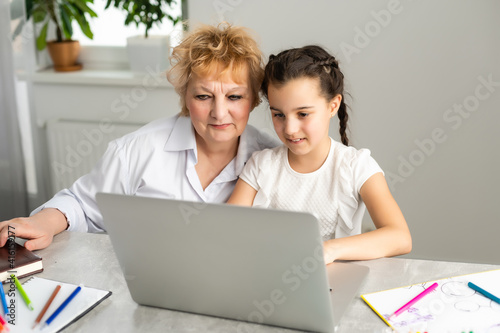 Grandmother teaching to granddaughter with the help of the computer. Worried old teacher helping girl studying and doing homework on laptop at home, private lesson