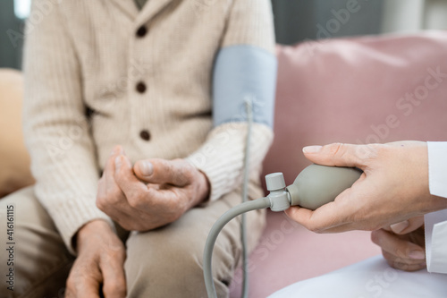 Hand of young doctor pressing pump of tonometer while measuring blood pressure