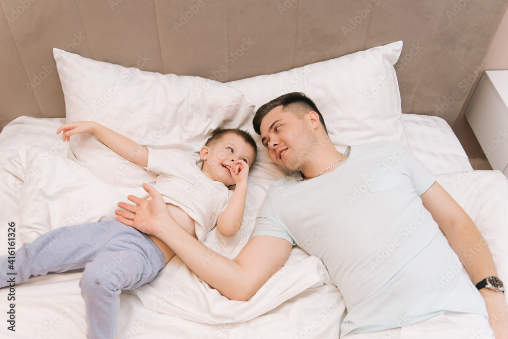 Young dad playing and laughing with his baby smiling son at home in bed in the bedroom, happy family Young dad playing and laughing with his baby smiling son at home in bed in the bedroom, happy family