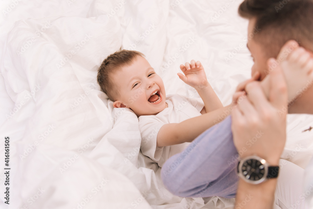 Young dad playing and laughing with his baby smiling son at home in bed in the bedroom, happy family Young dad playing and laughing with his baby smiling son at home in bed in the bedroom, happy family