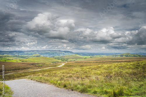Footpath or trail winding between green hills and peatbog with stormy, dramatic sky in background, Cuilcagh Mountain Park, Northern Ireland