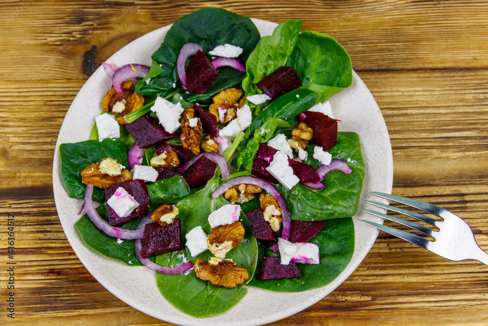 Tasty spinach salad with boiled beetroot, feta cheese, walnut and red onion on wooden table. Top view. Healthy vegetarian food Tasty spinach salad with boiled beetroot, feta cheese, walnut and red onion on wooden table. Top view. Healthy vegetarian food