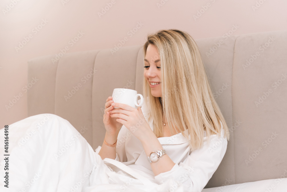 Beautiful young blonde smiling girl with coffee in a white bed, good morning Beautiful young blonde smiling girl with coffee in a white bed, good morning