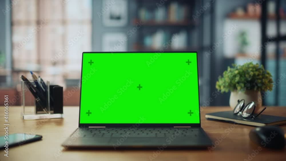 Laptop Computer with Mock Up Green Screen Display Standing on the Table in Cozy Living Room. In the Background Stylish Modern Bright Home Office Studio During Day with Big Cityscape Window.