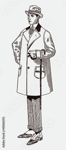 Adult man from early 20th century wearing balmaroon overcoat and hat, holding walking cane