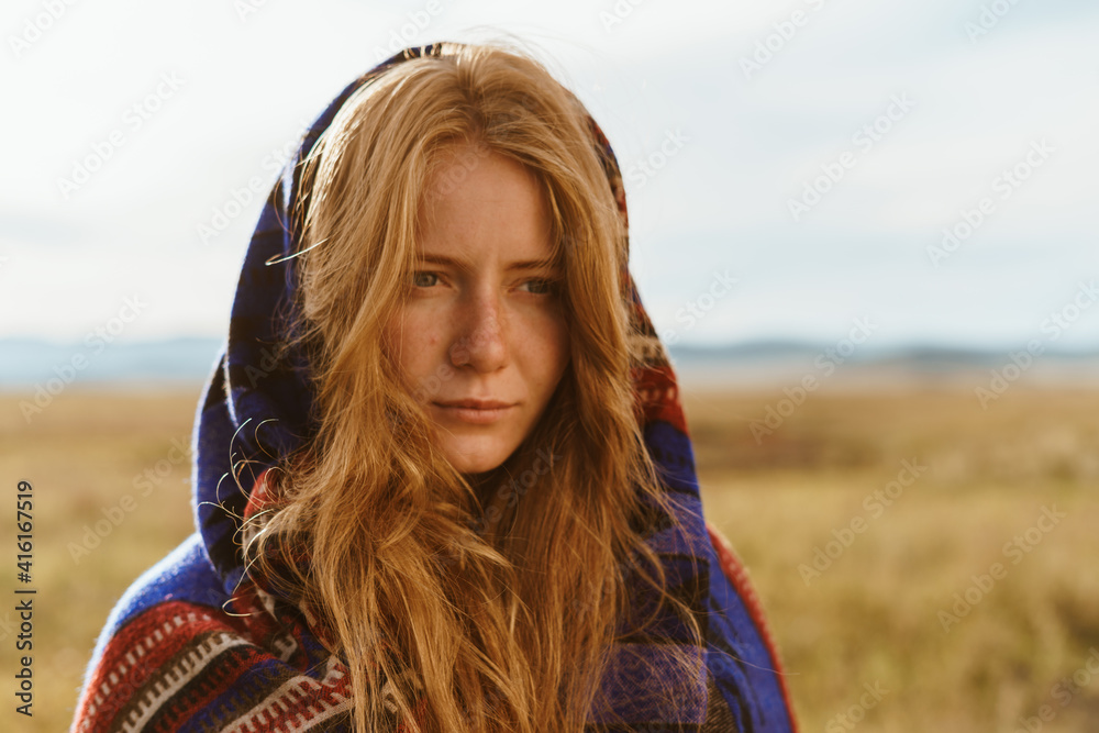 In the steppe stands a girl in an ethno cape with long loose hair without makeup with natural beauty. High quality photo