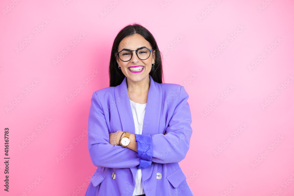 Young business woman wearing purple jacket over pink background with a happy face standing and smiling with a confident smile showing teeth with arms crossed Young business woman wearing purple jacket over pink background with a happy face standing and smiling with a confident smile showing teeth with arms crossed