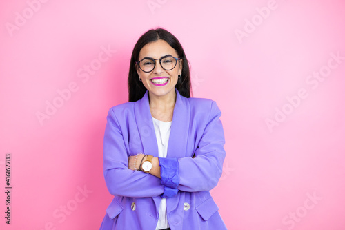 Young business woman wearing purple jacket over pink background with a happy face standing and smiling with a confident smile showing teeth with arms crossed