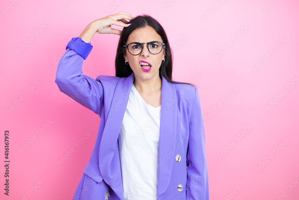 Young business woman wearing purple jacket over pink background confuse and wonder about question. Uncertain with doubt, thinking with hand on head