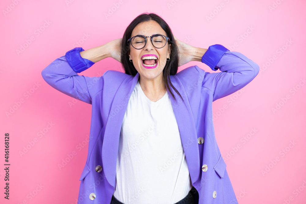 Young business woman wearing purple jacket over pink background relaxing and stretching, arms and hands behind head and neck smiling happy Young business woman wearing purple jacket over pink background relaxing and stretching, arms and hands behind head and neck smiling happy