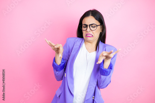 Young business woman wearing purple jacket over pink background disgusted expression, displeased and fearful doing disgust face because aversion reaction. Annoying concept photo