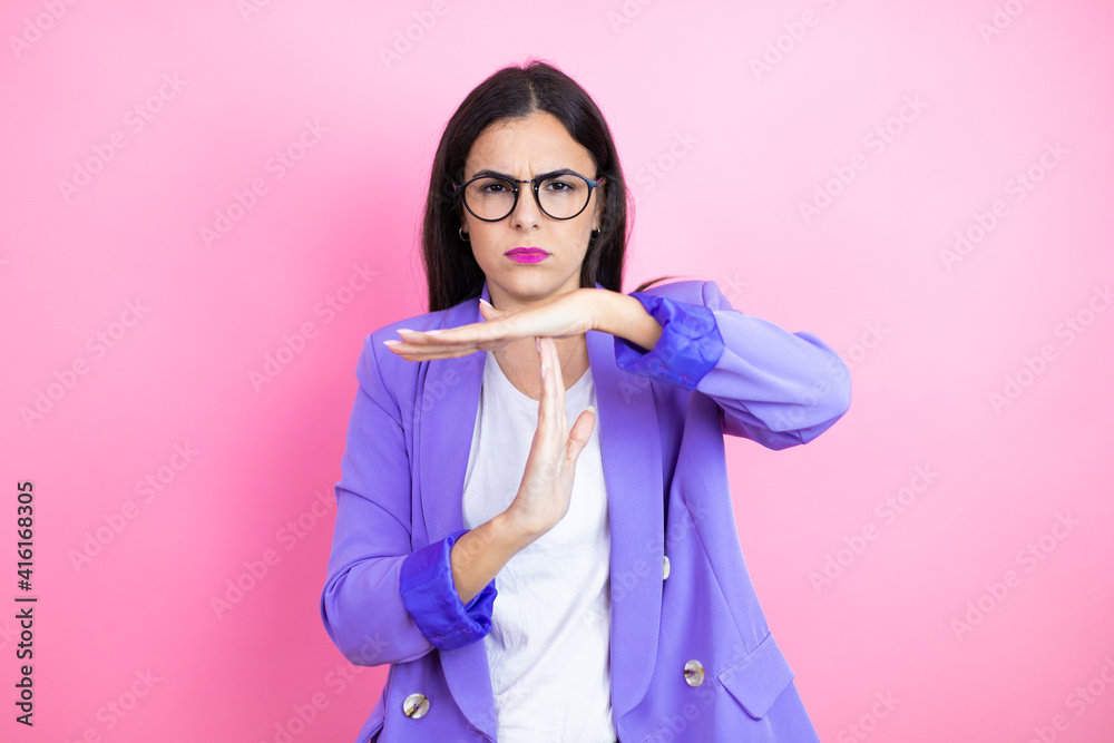 Young business woman wearing purple jacket over pink background Doing time out gesture with hands, frustrated and serious face Young business woman wearing purple jacket over pink background Doing time out gesture with hands, frustrated and serious face