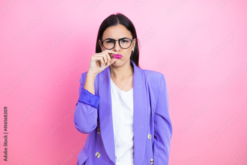 Young business woman wearing purple jacket over pink background mouth and lips shut as zip with fingers. Secret and silent, taboo talking