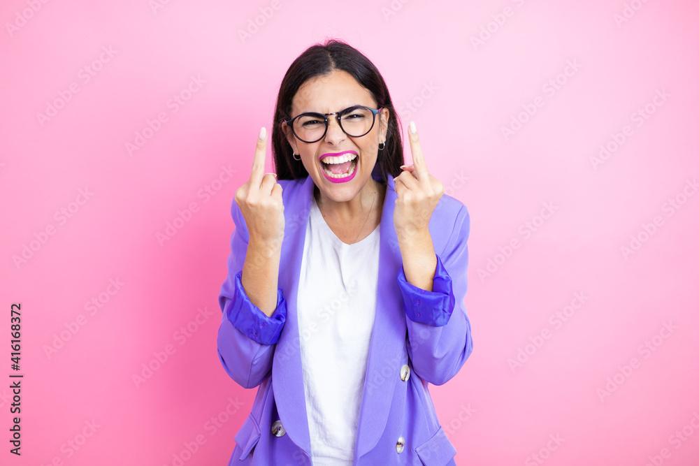 Young business woman wearing purple jacket over pink background showing middle finger doing fuck you bad expression, provocation and rude attitude. screaming excited