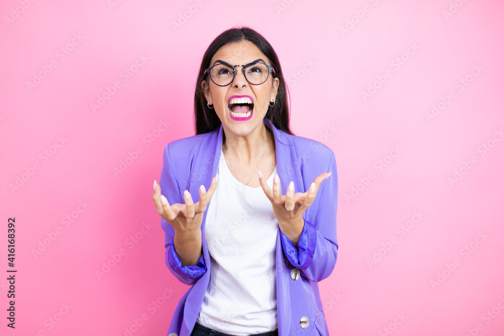 Φωτογραφία Young business woman wearing purple jacket over pink background crazy and mad shouting and yelling with aggressive expression and arms raised