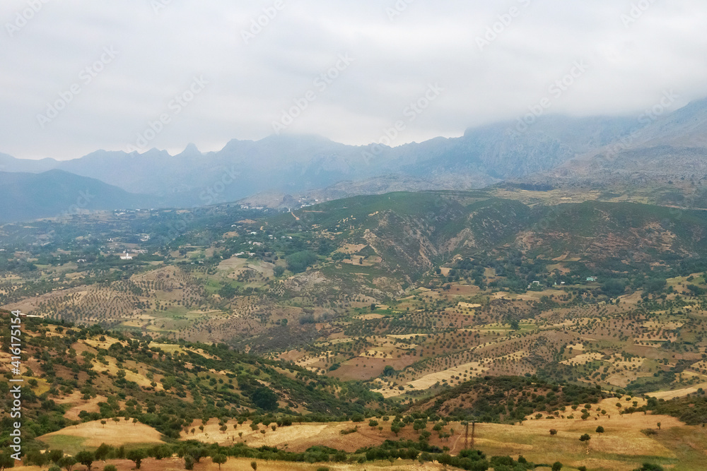 Moroccan landscape with foggy mountains and fields.