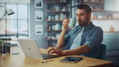 Handsome Caucasian Man Working on Laptop Computer while Sitting on a Sofa Couch in Stylish Cozy Living Room