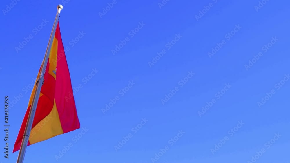 The flag of Spain against a clear blue sky with copy space.