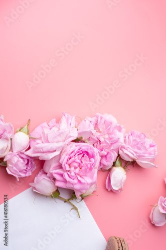 pink roses with white envelope and macaroons around pink background. life style concept. flat lay