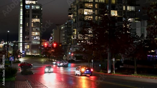 Cars stopping for a red traffic light waiting till it changed to green and proceed there trip over an intersection in downtown Vancouver between skyscrapers. Timelapse by night