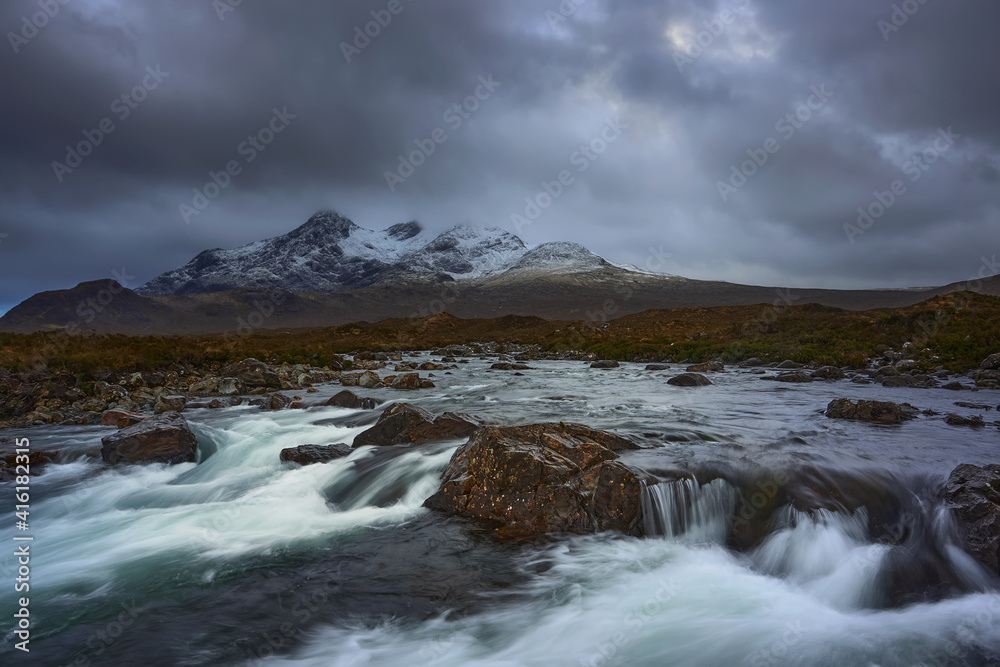 Long exposure of water over rocks and small waterfall on the River Sligachan on the Isle of Skye Scotland with the Cuillin mountain range in the distance with snow in winter, Isle of Skye, Scotland