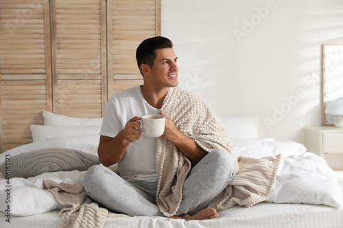 Man covered with plaid enjoying hot morning drink on bed indoors © New Africa