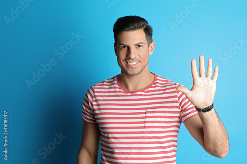 Man showing number five with his hand on light blue background