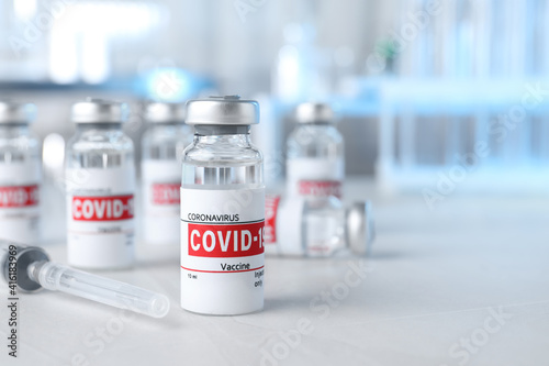 Glass vials with COVID-19 vaccine and syringe on light table. Space for text