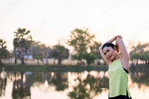 Young beautiful Asian woman in sports outfits doing stretching before workout outdoor in the park in the morning to get a healthy lifestyle. Healthy young woman warming up outdoors.