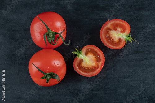 Two whole fresh tomatoes with slices on a dark background