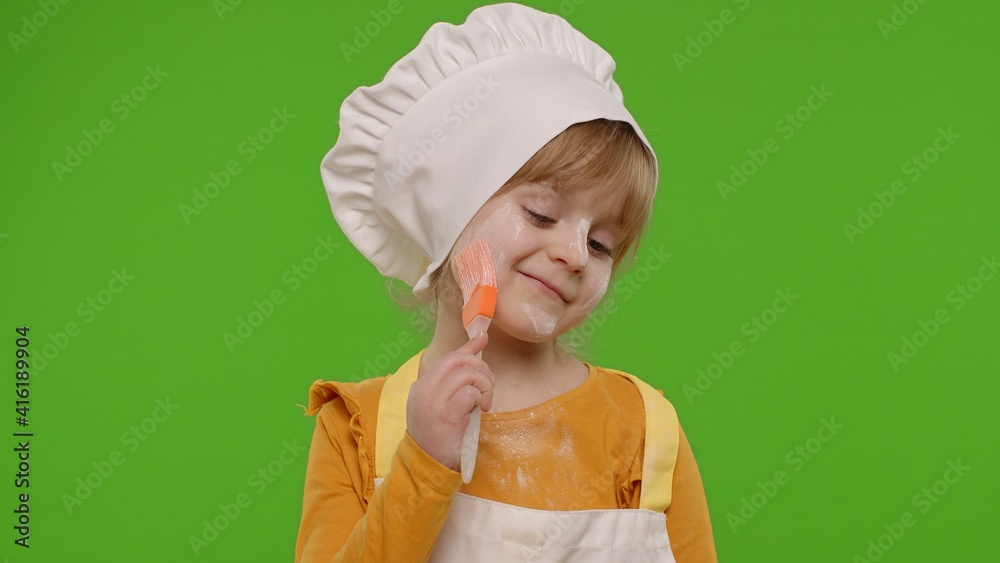 Caucasian preschooler child girl dressed as cook chef baker in apron smears face with flour, fooling around, making silly funny faces, showing tongue. Isolated on chroma key background. Copy-space Caucasian preschooler child girl dressed as cook chef baker in apron smears face with flour, fooling around, making silly funny faces, showing tongue. Isolated on chroma key background. Copy-space