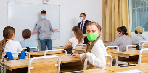 Portrait of diligent schoolgirl wearing protective face mask sitting in class working with classmates, new normal education during pandemic