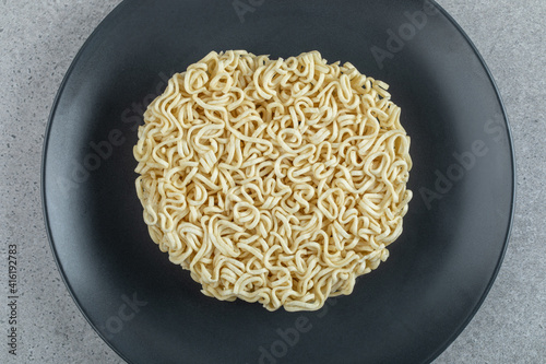 Black plate of unprepared noodles on a gray background photo